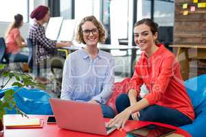 Smiling business executives sitting in office with laptop on table