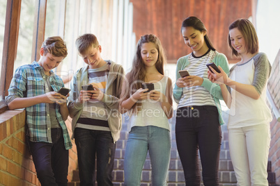 Group of smiling school friends using mobile phone in corridor