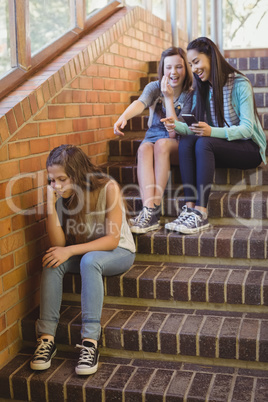 School friends bullying a sad girl in school corridor
