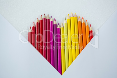 Colored pencils arranged in heart shape on white background