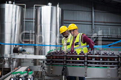 Factory workers monitoring cold drink bottles at drinks production plant