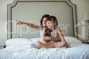 Mother with daughter pointing at a distance on bed