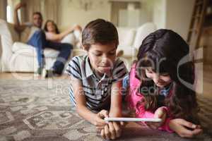 Sibling lying on rug and using digital tablet in living room