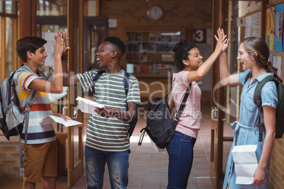 Happy classmates giving high five to each other in corridor