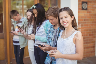 Group of smiling school friends using mobile phone in corridor