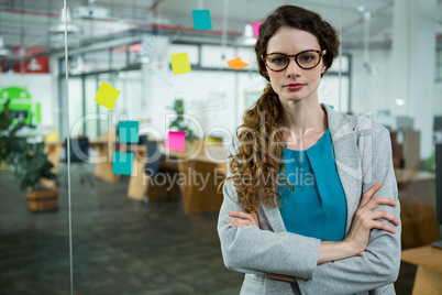 Confident female executive standing with arms crossed in creative office