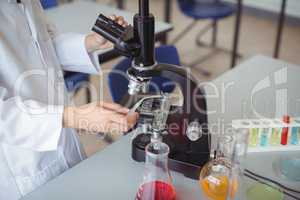 Mid section of schoolgirl experimenting on microscope in laboratory