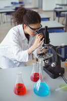 Attentive schoolgirl looking through microscope in laboratory