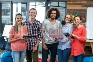 Smiling business executives standing in office with digital tablet and laptop