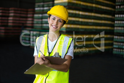 Smiling female factory worker writing on clipboard in factory