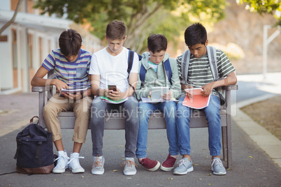 School kids using mobile phone and digital tablet on bench