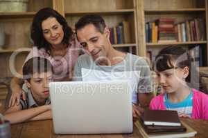 Parents and kids using laptop on table in study room