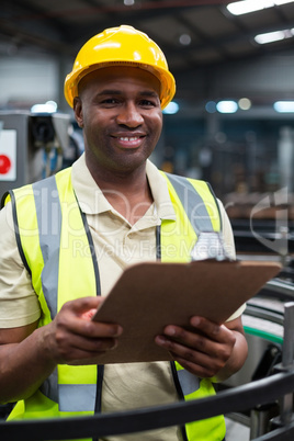 Smiling factory worker holding clipboard in factory