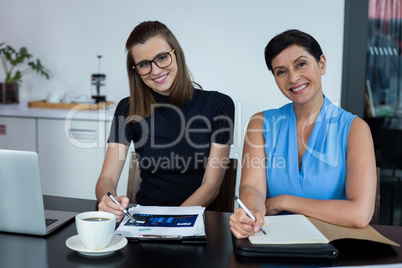 Portrait of smiling business executives discussing over clipboard at meeting