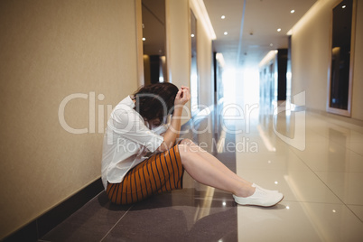 Sad female business executive sitting in corridor