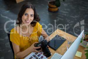 Smiling graphic designer holding digital camera in creative office