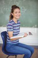 Portrait of schoolgirl sitting on chair and holding a book in classroom