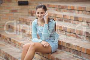 Happy schoolgirl sitting on staircase and talking mobile phone