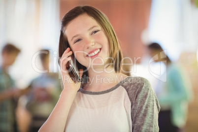 Smiling schoolgirl talking on mobile phone in corridor