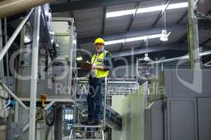 Male factory worker maintaining record on clipboard