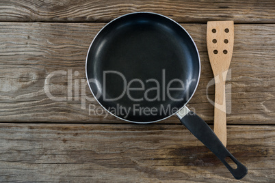 Pan and wooden spatula against wooden background