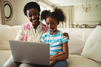 Portrait of mother and daughter using laptop in living room