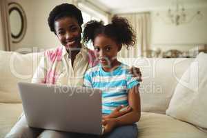 Portrait of mother and daughter using laptop in living room