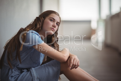 Thoughtful schoolgirl sitting in corridor