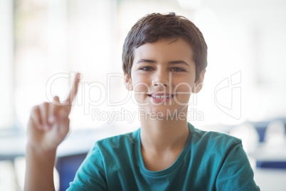 Portrait of happy schoolboy raising hand in classroom