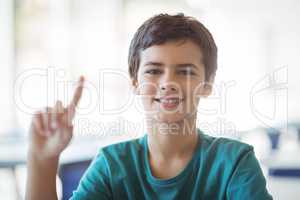 Portrait of happy schoolboy raising hand in classroom