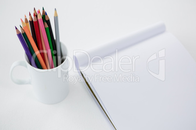 Colored pencils kept in mug with notepad
