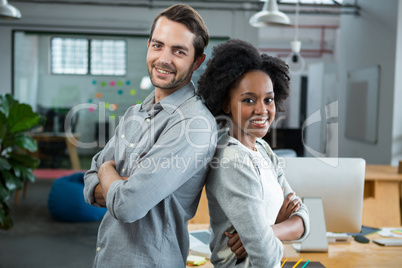 Happy man and woman standing back to back in office