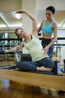 Female trainer assisting woman with stretching exercise on reformer