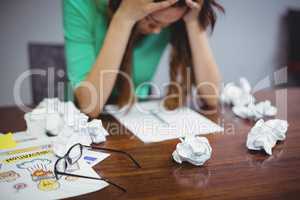 Frustrated female business executive sitting with crumpled papers balls