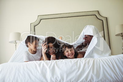 Happy family lying under blanket on bed at home
