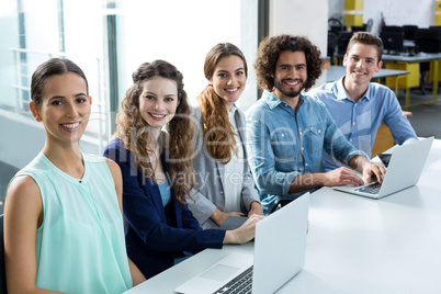 Portrait of smiling business team discussing over laptop in meeting