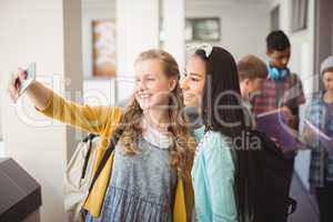 Smiling schoolgirls taking selfie with mobile phone in corridor