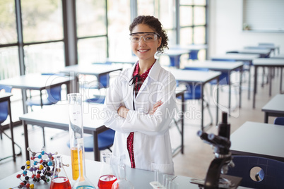 Portrait of schoolgirl in lab coat standing with arms crossed in laboratory