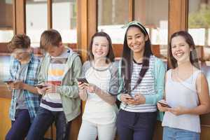 Portrait of smiling school friends using mobile phone in corridor