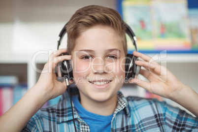 Portrait of happy schoolboy listening music on headphones in library
