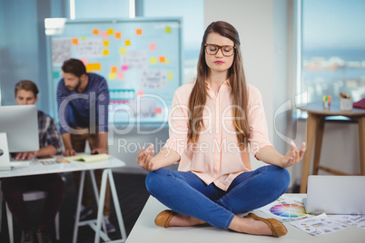 Female graphic designer sitting on table and meditating