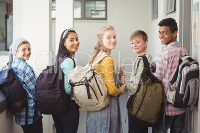 Portrait of smiling students standing with notebook and school bag in corridor