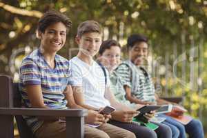 School kids using mobile phone and digital tablet on bench in school campus