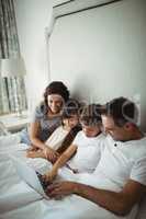 Parents and kids using laptop in bed