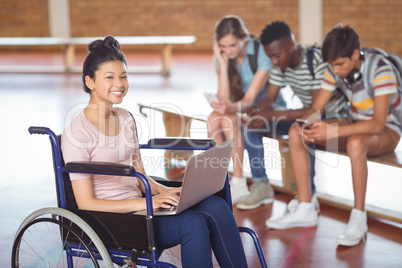 Portrait of disabled schoolgirl using laptop with classmates in background