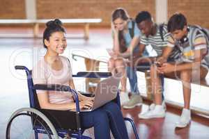 Portrait of disabled schoolgirl using laptop with classmates in background
