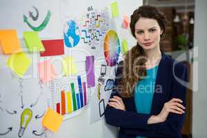Confident female executive standing with arms crossed in creative office