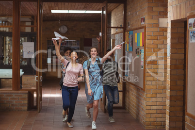Excited classmates running with grade cards in corridor