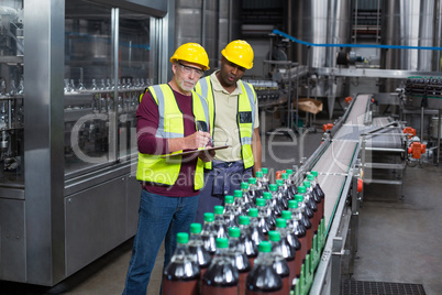 Two factory workers monitoring cold drink bottles in the plant