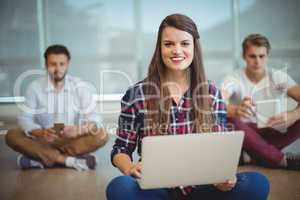 Portrait of female business executives sitting on floor and using laptop
